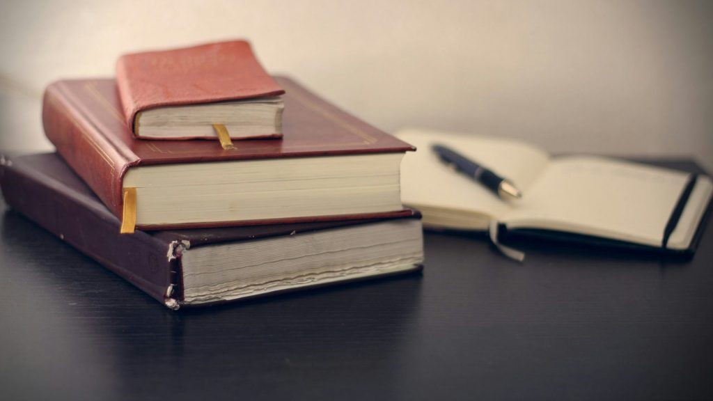 Fotografía de enfoque selectivo de tres libros junto a un cuaderno abierto.