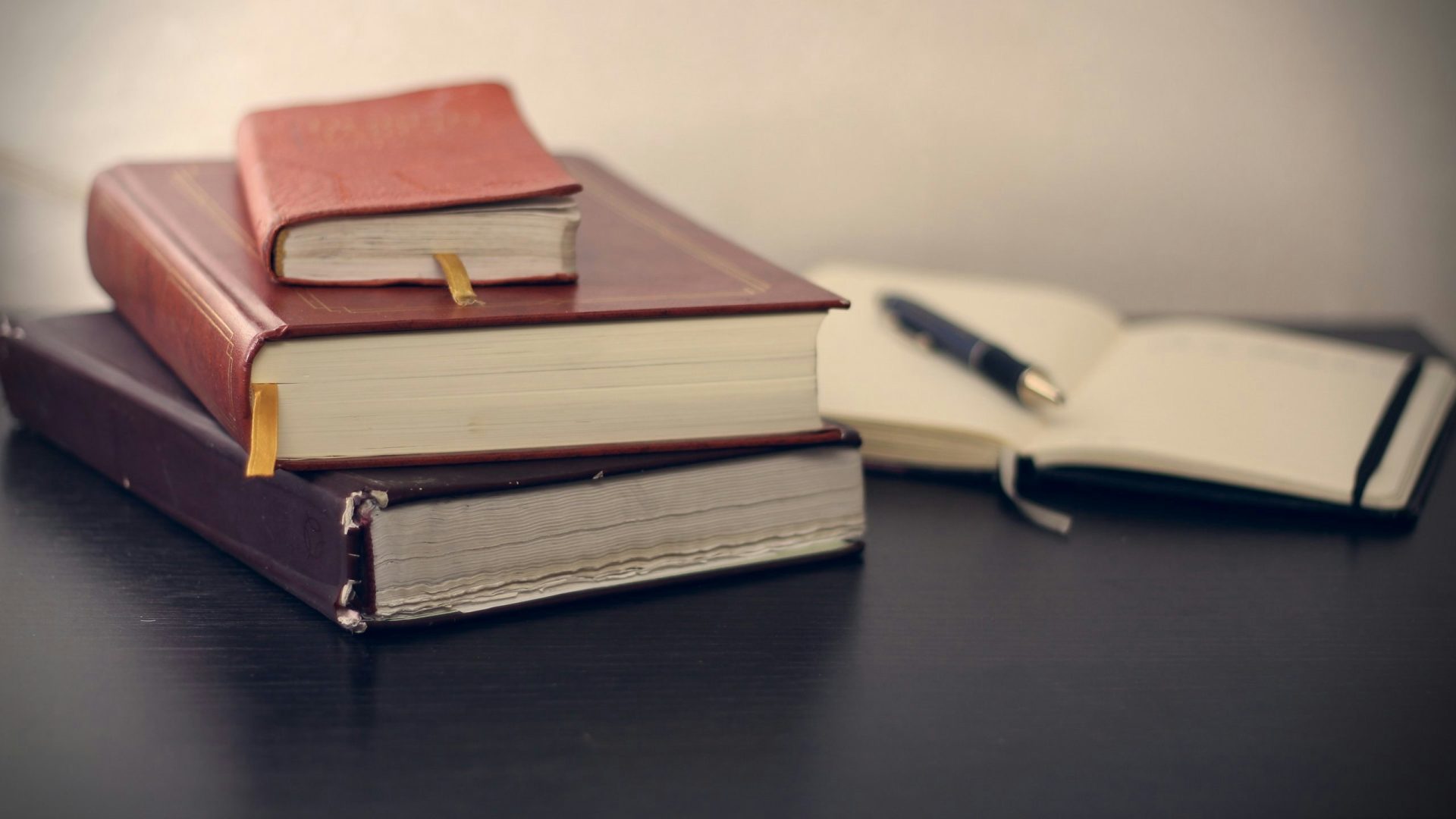 Fotografía de enfoque selectivo de tres libros junto a un cuaderno abierto.