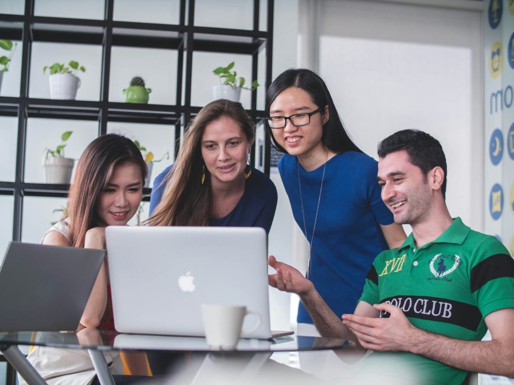 Cuatro personas mirando en una MacBook blanca encima de una mesa de cristal
